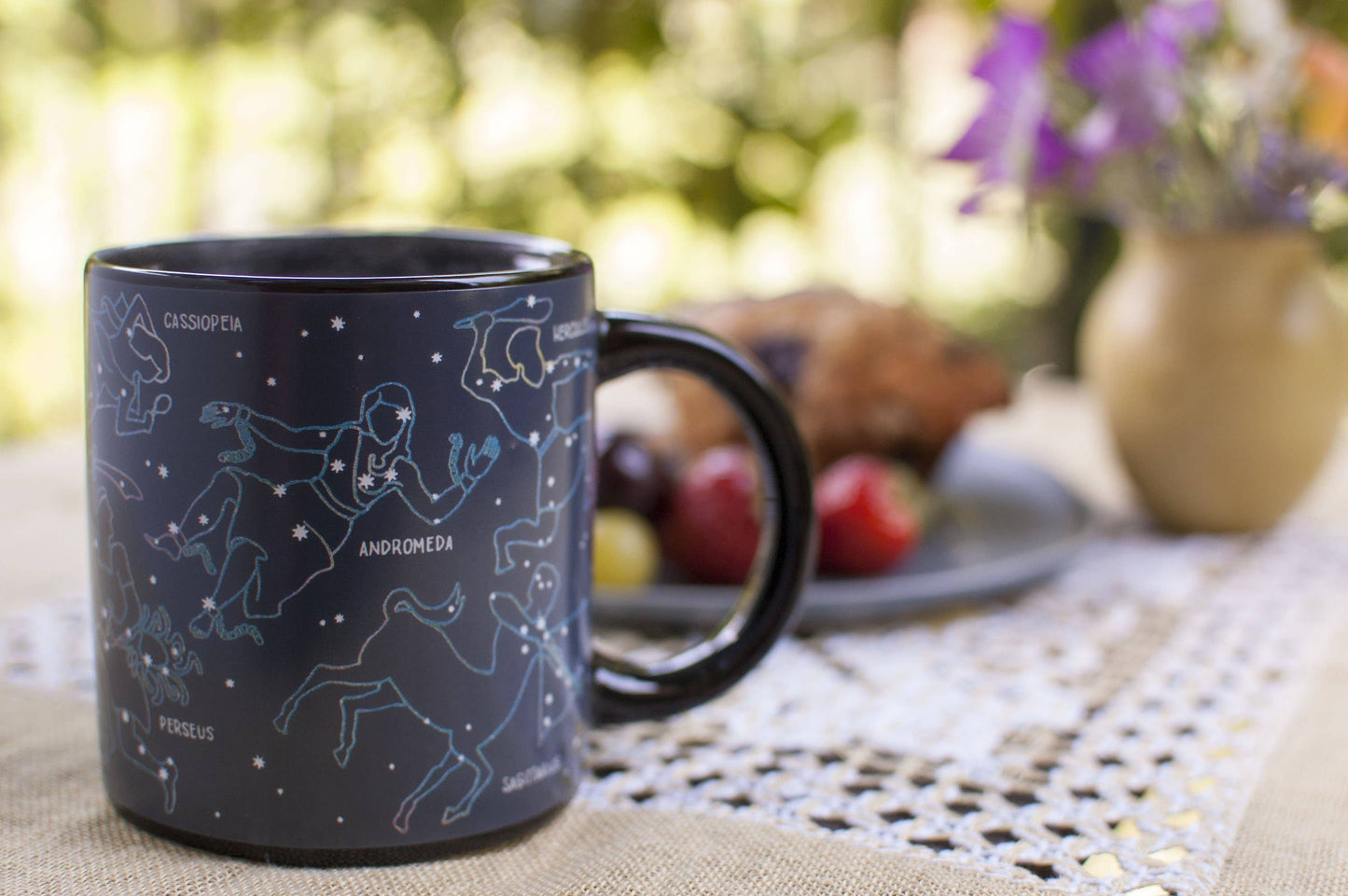 Heated constellation coffee mug on table with fruit and muffin and flowers