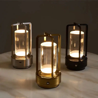 Three Crystal Lanterns with lights inside, placed on a table. The lanterns have clear glass tops and bases with metallic frames in gold, silver, and black colors.