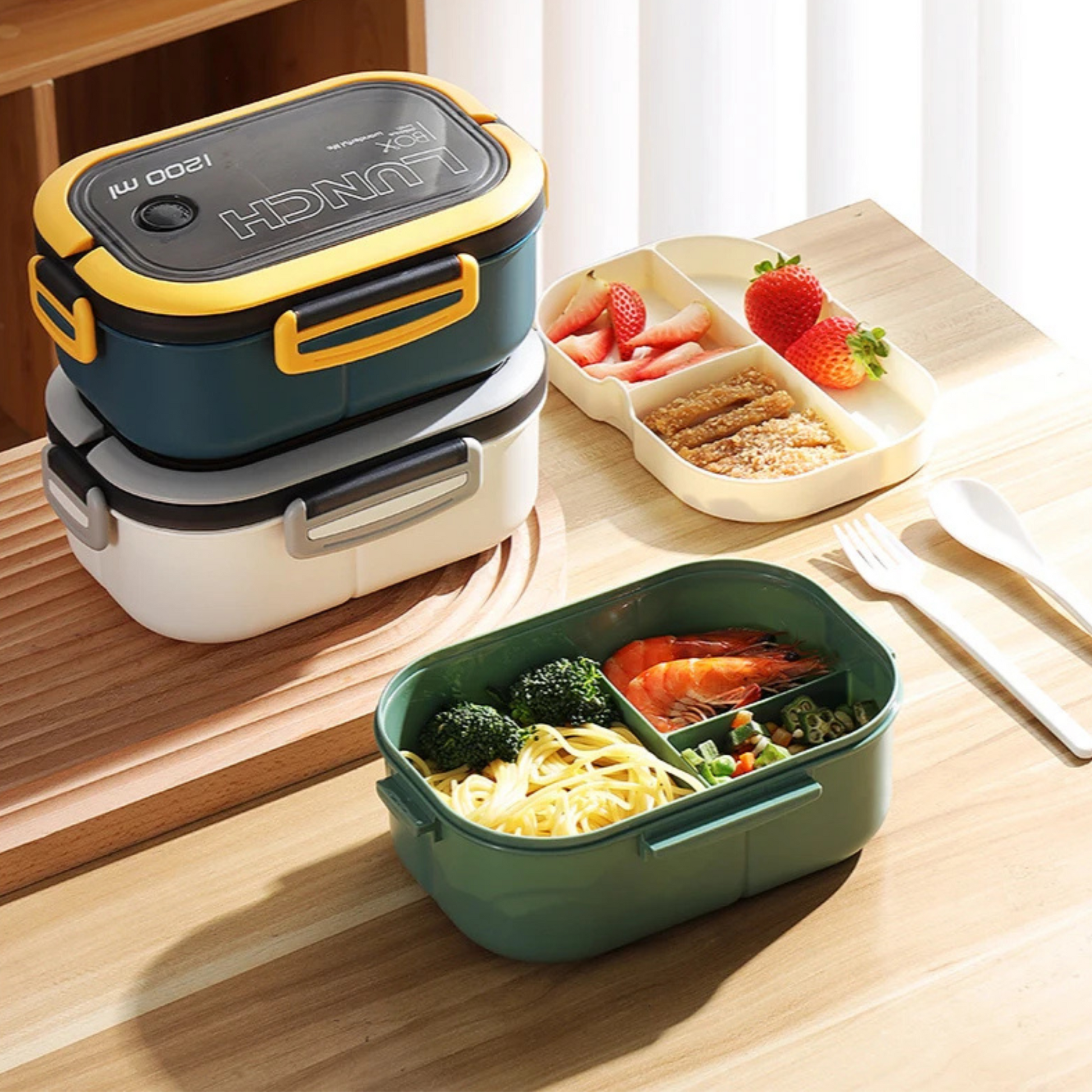 White and blue lunch boxes closed with green lunch box open showing layers and utensils