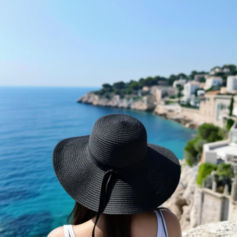 Black foldable straw hat with wide brim worn by woman at the beach – sun-ready and chic