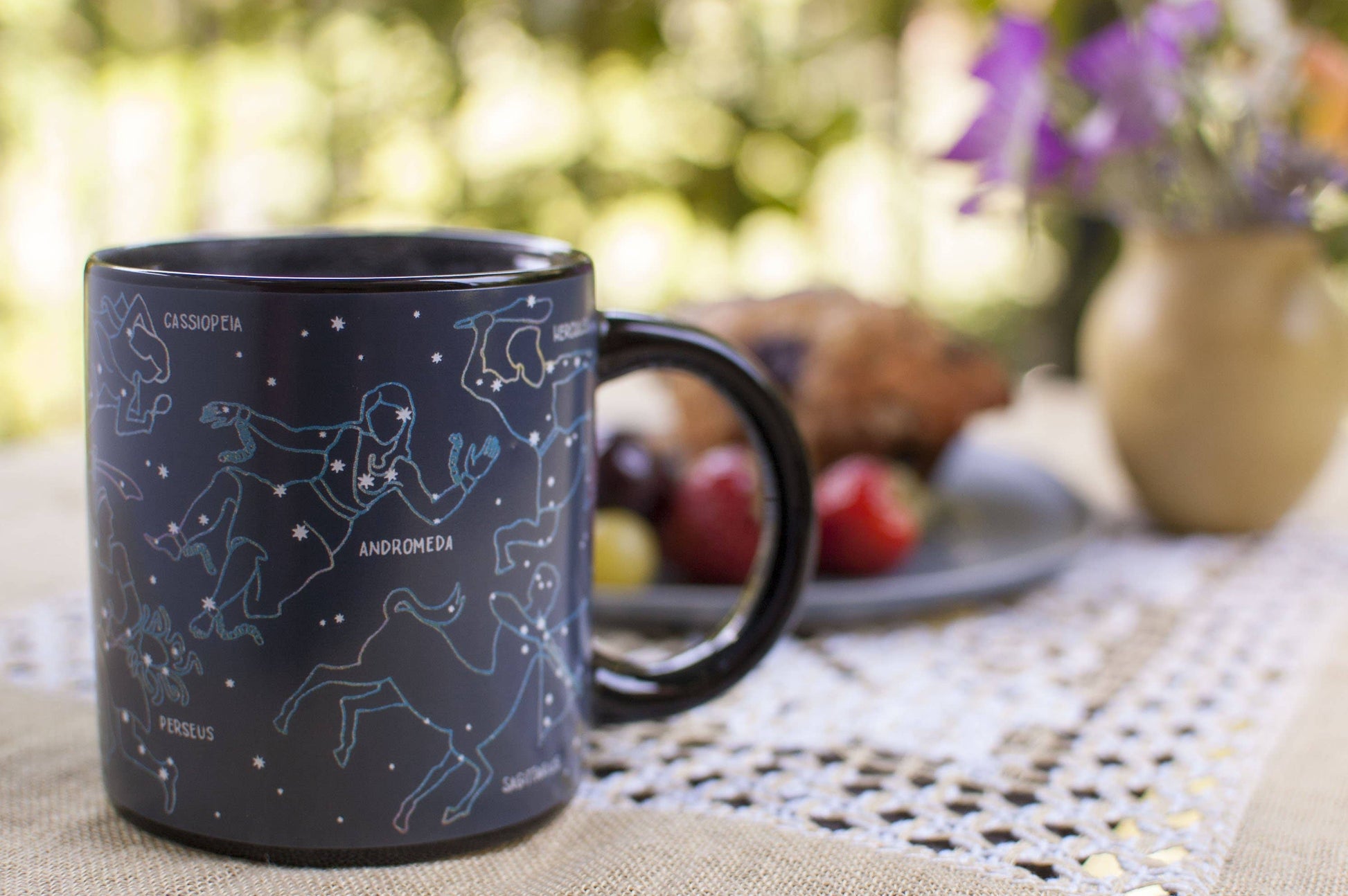 Heated constellation coffee mug on table with fruit and muffin and flowers