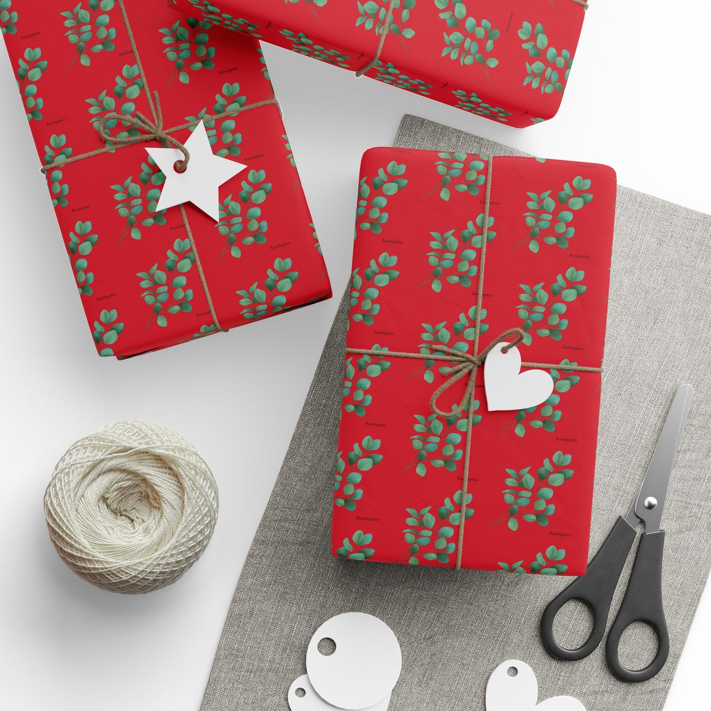 Three gifts wrapped in eucalyptus-themed paper with scissors and gift labels